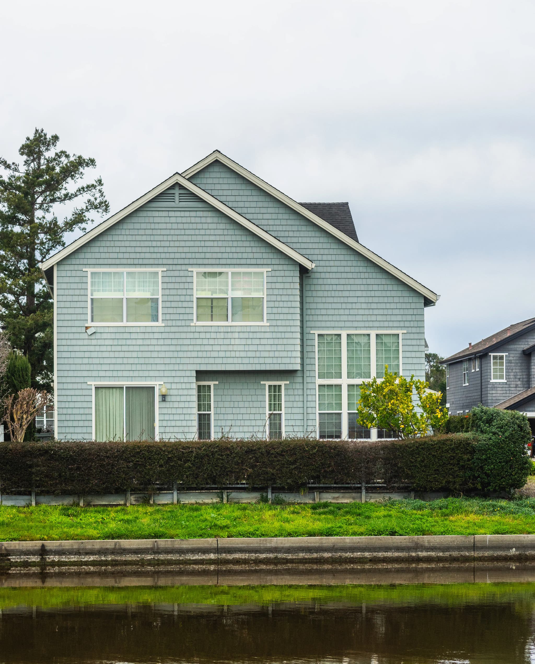 Two-storey house with a pale blue-grey exterior behind a trimmed hedge