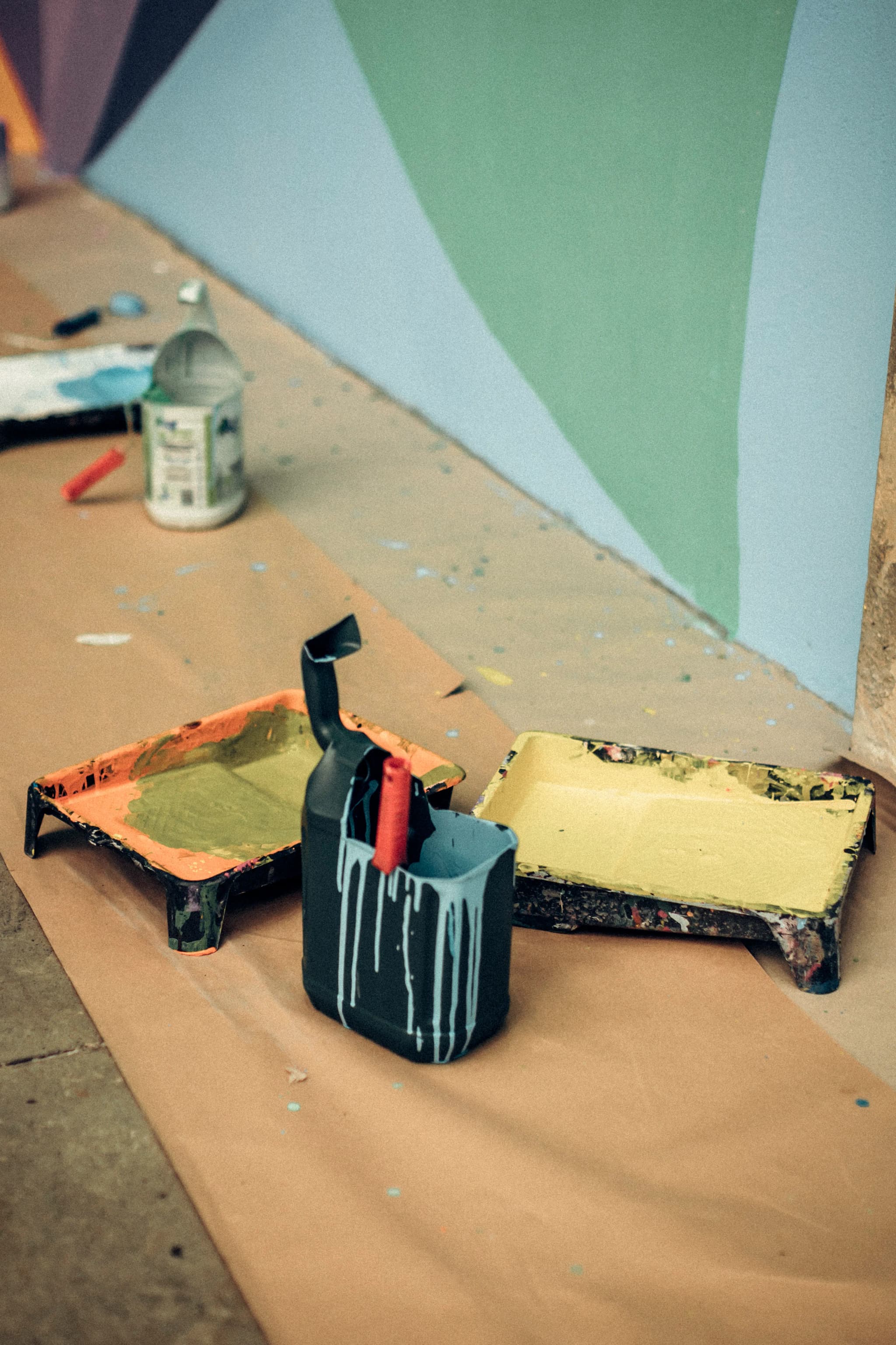 Paint trays and a brush pot on floor paper in front of a wall painted pale blue and sage green