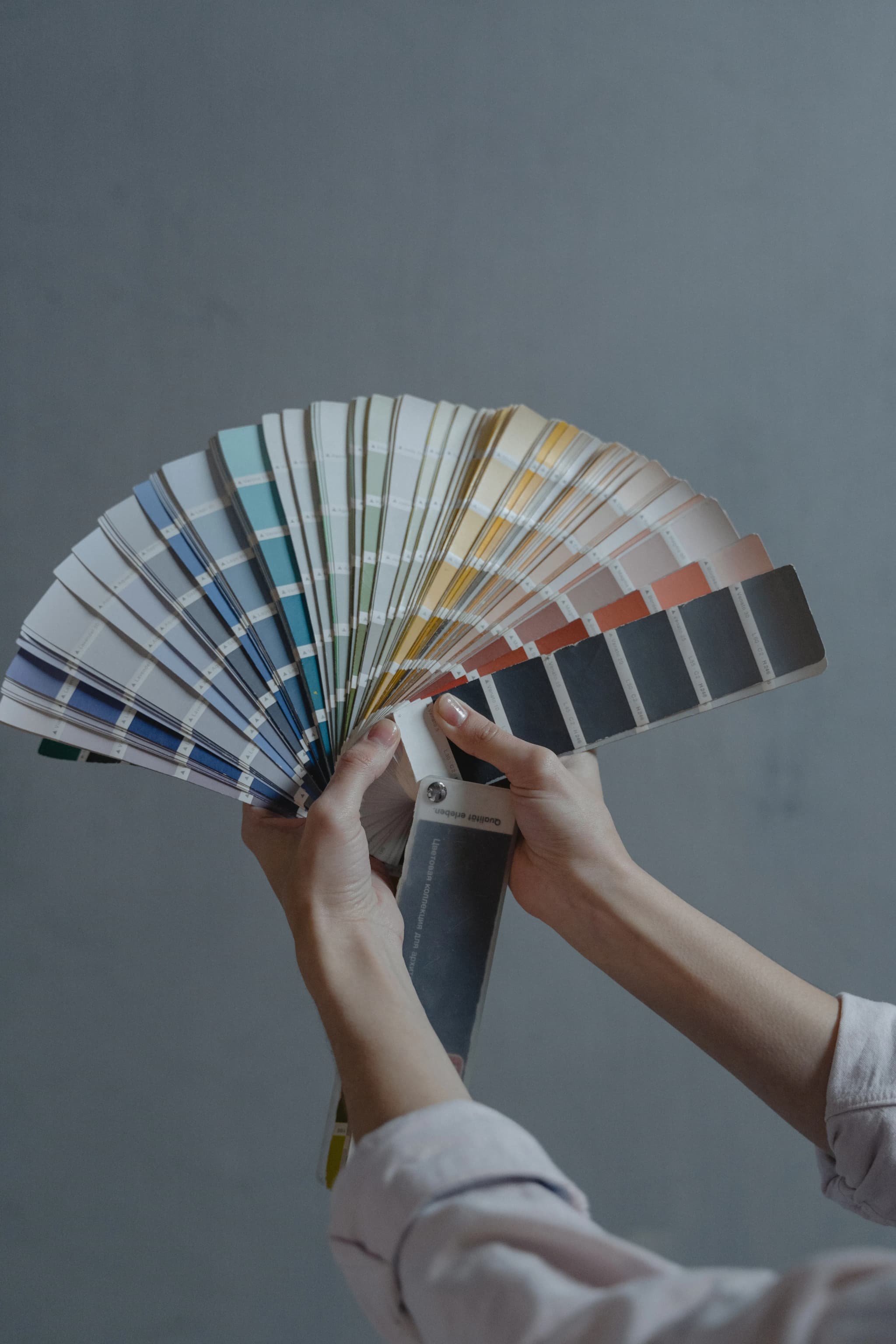 Hands holding a fan of paint colour swatches against a wall