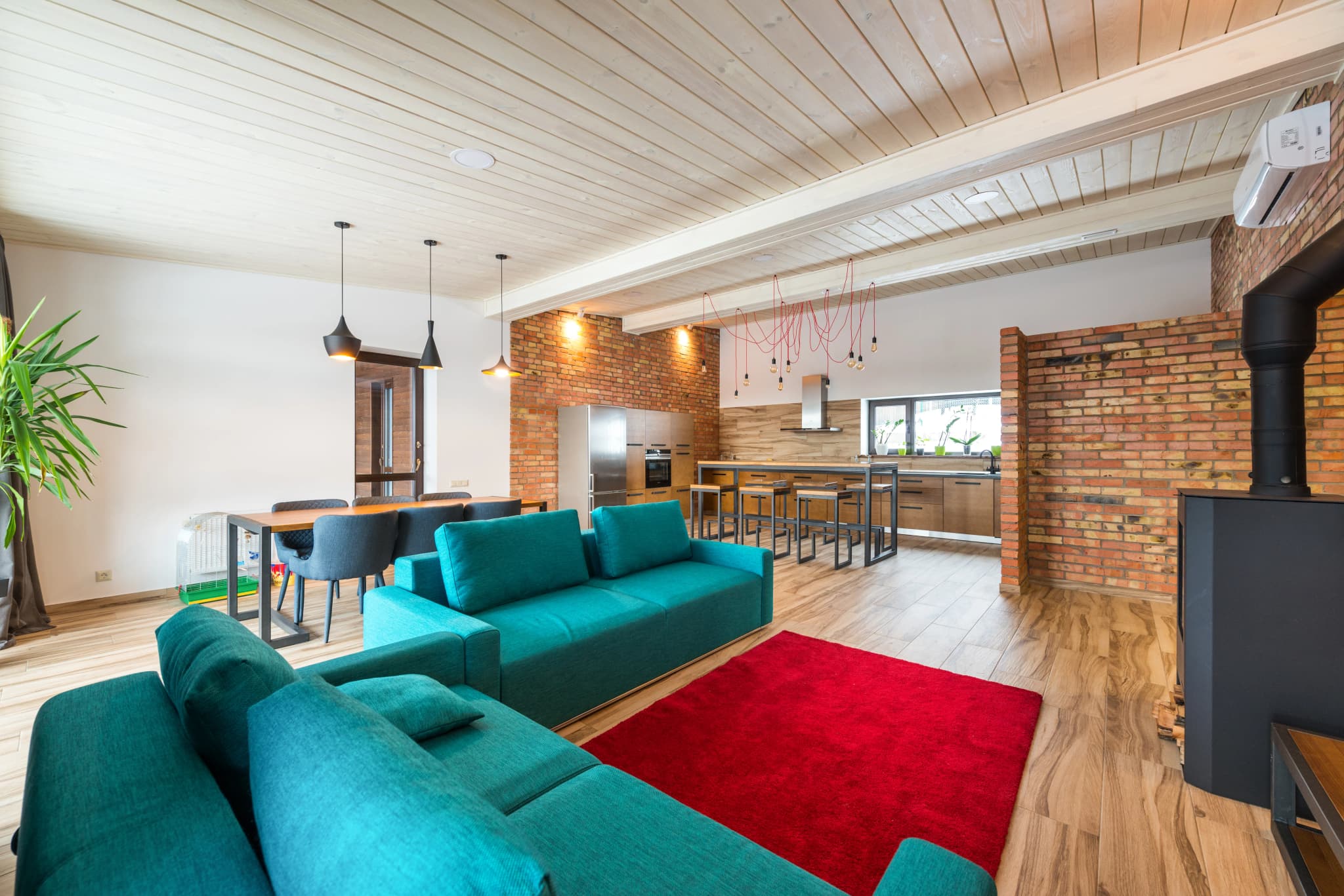 Open-plan living room with teal sofas, white walls and exposed brick
